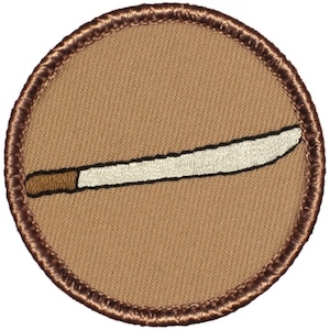 May include: A brown embroidered patch with a white and brown machete on a tan background.