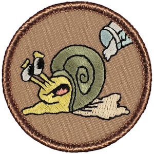 May include: A brown embroidered patch with a cartoon snail with a green shell and a white bucket behind it.