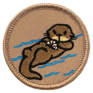 May include: A brown embroidered patch of a cartoon sea otter floating on its back in blue water. The patch is circular and has a tan background.