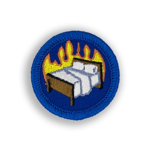 May include: A blue embroidered patch with a bed on fire. The bed is brown with white sheets and pillows. The flames are yellow and orange.