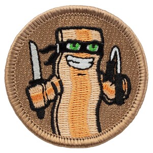 May include: A round, tan embroidered patch with a cartoon image of a smiling, striped bacon character wearing a black eye mask and holding a knife in one hand and a gun in the other.