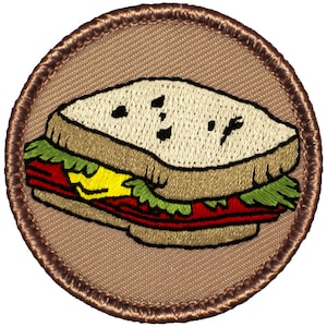 May include: A brown embroidered patch with a cartoon image of a sandwich. The sandwich is filled with lettuce, tomato, and cheese.