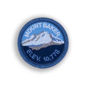 May include: A blue and white embroidered patch with the text "MOUNT BAKER ELEV. 10,778" and a depiction of a snow-capped mountain.