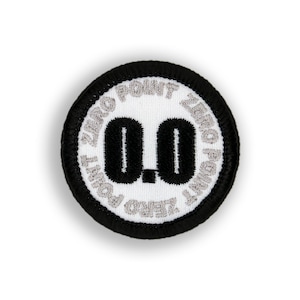 May include: A white round patch with black embroidery. The text "ZERO POINT ZERO" is embroidered in silver around the edge of the patch. The number "0.0" is embroidered in black in the center of the patch.