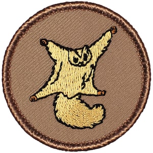 May include: A brown embroidered patch with a yellow sugar glider with its wings spread out. The sugar glider is facing forward with its tail curled behind it.
