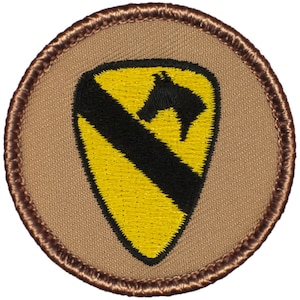 May include: A round, brown patch with a yellow and black embroidered shield. The shield features a black silhouette of a horse's head with a black diagonal stripe across the shield.