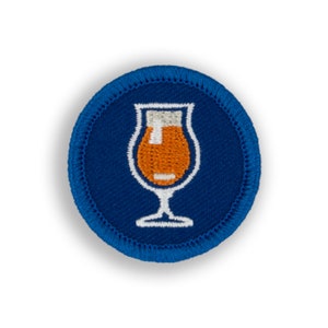 May include: A blue and white embroidered patch with a glass of beer. The glass is filled with orange liquid and has a white foam head.