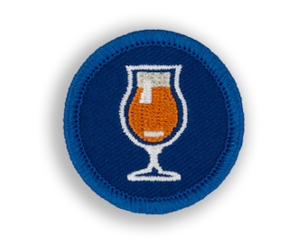 May include: A blue and white embroidered patch with a glass of beer. The glass is filled with orange liquid and has a white foam head.