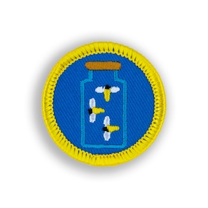 May include: Embroidered patch featuring a blue jar with three stylized bees inside. The jar has a brown top and is set against a blue background. The patch is round with a yellow border.