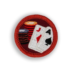 May include: A red, white, and black embroidered patch with a stack of poker chips and two playing cards, one showing an ace of hearts and the other an ace of spades.