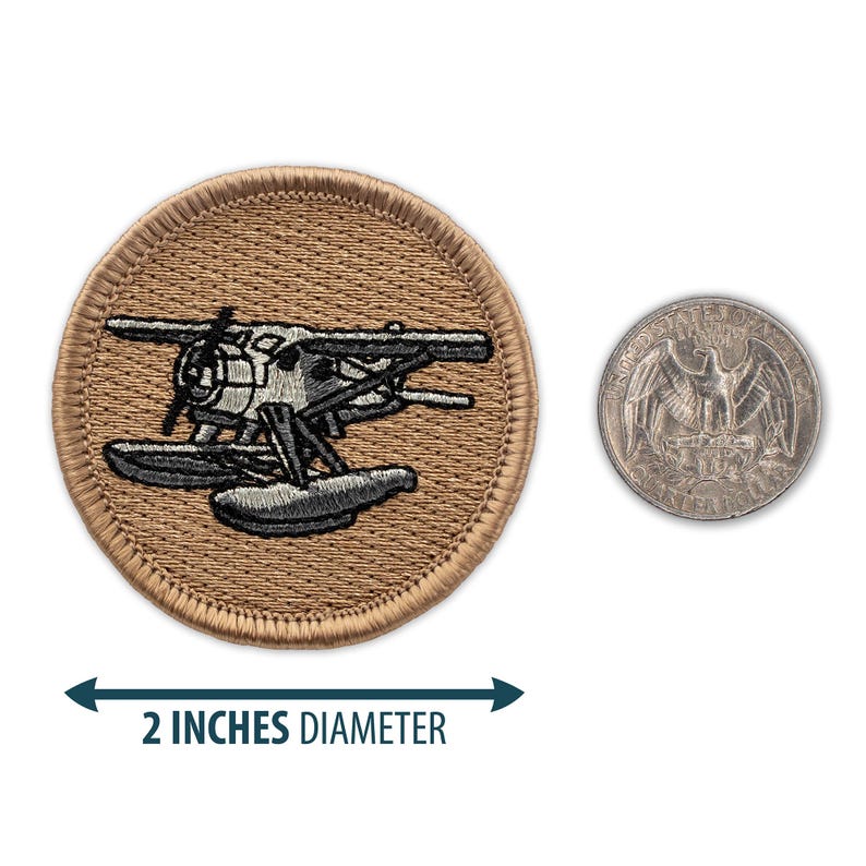 May include: A 2-inch diameter embroidered patch featuring a gray and white seaplane on a tan background. The patch is shown next to a US quarter for size comparison.