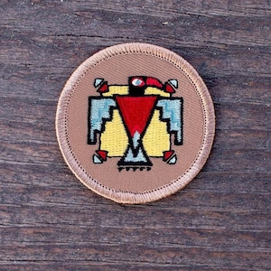 May include: A round, tan fabric patch with a colorful embroidered Native American design of a bird with a red, yellow, and blue pattern.