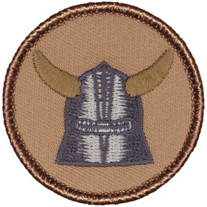 May include: A brown embroidered patch with a gray and white Viking helmet with horns. The patch has a brown border.