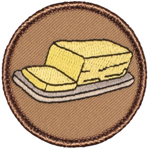 May include: A brown embroidered patch with a yellow stick of butter on a white dish.