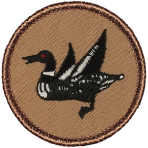May include: A brown embroidered patch with a black and white loon bird with a red eye. The patch has a brown border.