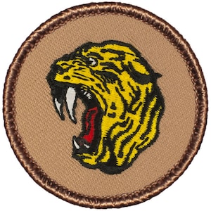 May include: A brown embroidered patch with a yellow and black tiger head with a red open mouth and large white fangs. The tiger is facing left and has a fierce expression.