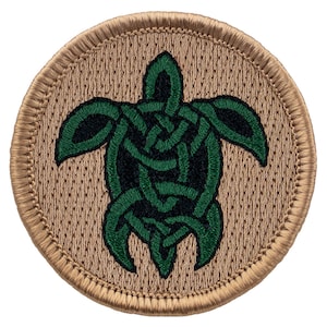 May include: Round patch featuring a green Celtic knot turtle design on a tan background. The turtle's intricate design is stitched in green thread, with a black center. The patch has a tan border.