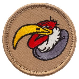 May include: A round, tan-colored patch with a cartoon-style red, white, and yellow bird with a large beak. The bird's head is turned to the left, and its beak is open. The patch has a brown stitched border.