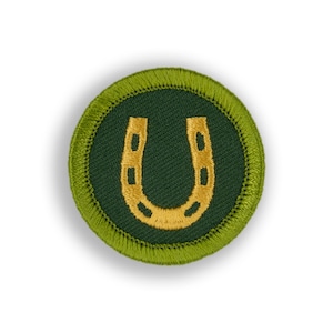 May include: A green and gold embroidered scout badge with a horseshoe design.