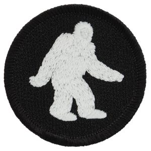 May include: White embroidered silhouette of Bigfoot on a black circular patch.