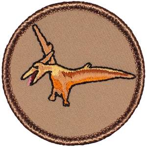May include: A brown embroidered patch with a cartoon image of a pterodactyl with a long neck and a long tail. The pterodactyl is orange and brown with a red tongue.
