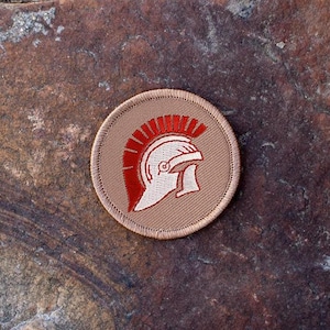 May include: A tan embroidered patch with a red and white Roman helmet design.