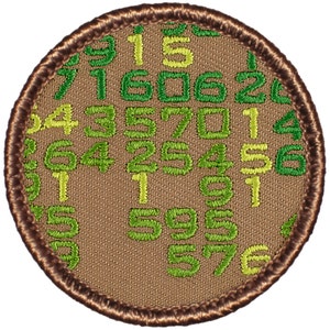May include: A brown embroidered patch with a green and yellow border. The patch is covered in a pattern of numbers.