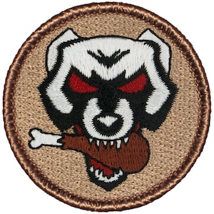 May include: A round, brown embroidered patch with a white cartoon dog with red eyes and a brown bone in its mouth. The dog is wearing a black collar.