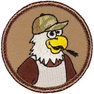 May include: A brown embroidered patch with a cartoon eagle wearing a camouflage hat and a brown jacket. The eagle has a yellow beak and a white beard.