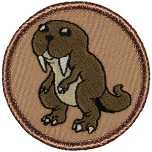 May include: A brown embroidered patch with a cartoon walrus wearing a dinosaur costume. The patch is circular and has a brown border.