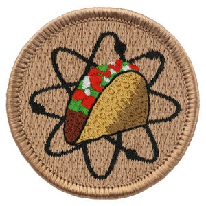 May include: A brown embroidered patch with a taco inside of an atom symbol. The taco is filled with meat, lettuce, tomato, and cheese.