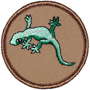 May include: A brown embroidered patch with a green gecko with pink spots on a tan background.