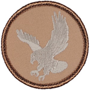 May include: A white embroidered eagle patch on a tan background with a brown border.