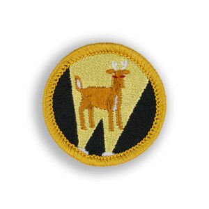 May include: A yellow and black embroidered patch with a deer in the center. The deer is brown with white markings and red eyes.