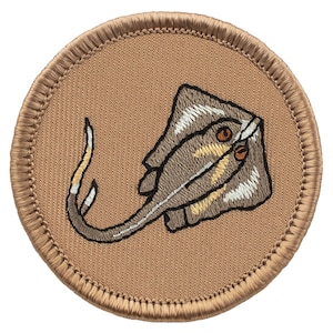 May include: Embroidered patch featuring a stylized stingray design. The patch is circular with a tan background and a detailed image of a stingray in shades of brown, tan, and white. The patch has a stitched border.