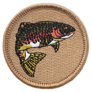 May include: Embroidered patch featuring a colorful trout fish on a brown background. The fish is depicted in a jumping pose with its tail raised.