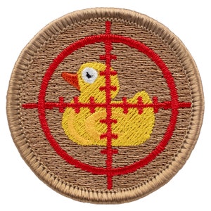 May include: A yellow rubber ducky is in the center of a red target with a brown background. The target has a red circle around the ducky and red lines extending from the center of the circle.