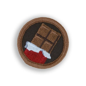 May include: A brown embroidered patch with a chocolate bar with a red and white wrapper. The patch is circular and has a brown border.