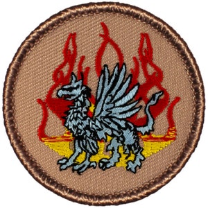 May include: A brown embroidered patch with a gray winged creature with a red and yellow flame design.
