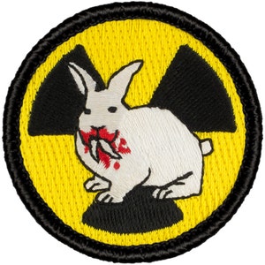 May include: A white rabbit with red blood on its mouth is biting a carrot inside a yellow and black radiation symbol.