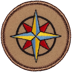 May include: A brown embroidered patch with a compass rose design. The compass rose is yellow, red, and blue with a black outline.