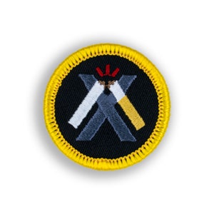 May include: A yellow embroidered patch with a black background and a white and yellow 'X' formed by two crossed cigarettes with red flames at the top.