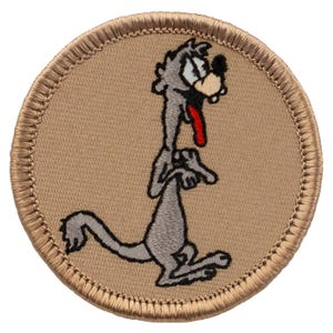 May include: A round, tan embroidered patch with a cartoon coyote with a red tongue sticking out. The coyote is standing on its hind legs with its front paws raised. The patch has a brown border.