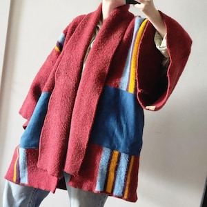 May include: A red, textured kimono-style jacket with blue, yellow, and purple accent stripes. The jacket has a shawl collar and wide sleeves. The front panels feature large blue patches. The garment is made of a thick, warm material, perfect for layering.