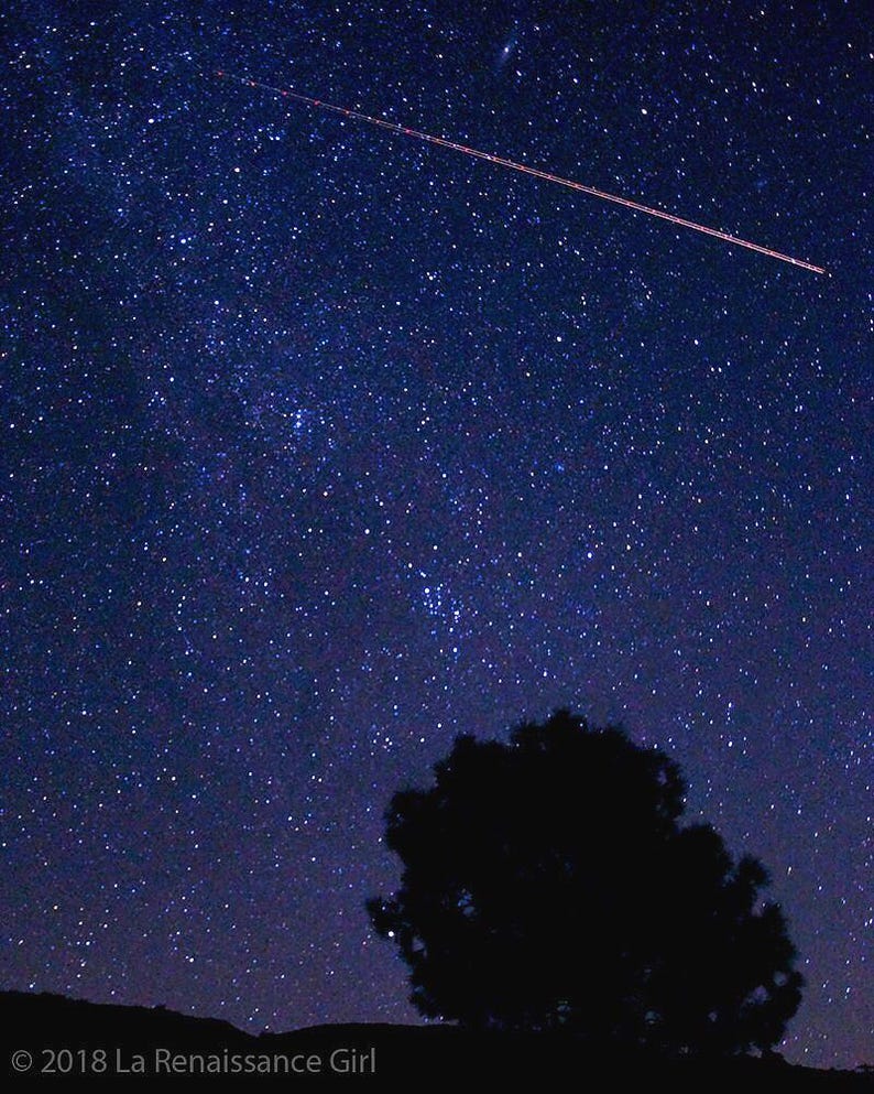May include: Night sky photograph featuring a dark blue expanse of stars. A bright streak of light crosses the frame diagonally. A dark silhouette of a tree and a hill are in the foreground. The image is labeled with the text "&copy; 2018 La Renaissance Girl."