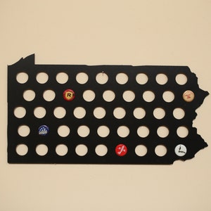 Peut inclure: Contour en m&eacute;tal noir de l'&eacute;tat de Pennsylvanie avec 49 d&eacute;coupes circulaires pour des capsules de bouteilles. Certaines des d&eacute;coupes sont remplies de capsules de bouteilles avec diff&eacute;rents logos et couleurs.