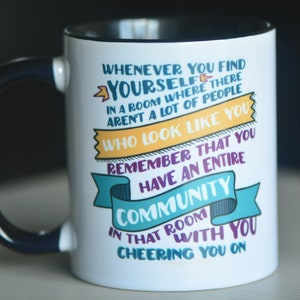 May include: White ceramic mug with a black handle. The mug features a colourful design with the text "Whenever you find yourself in a room where there aren't a lot of people who look like you, remember that you have an entire community in that room with you cheering you on."