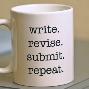 May include: White ceramic mug with black text that reads "write. revise. submit. repeat."
