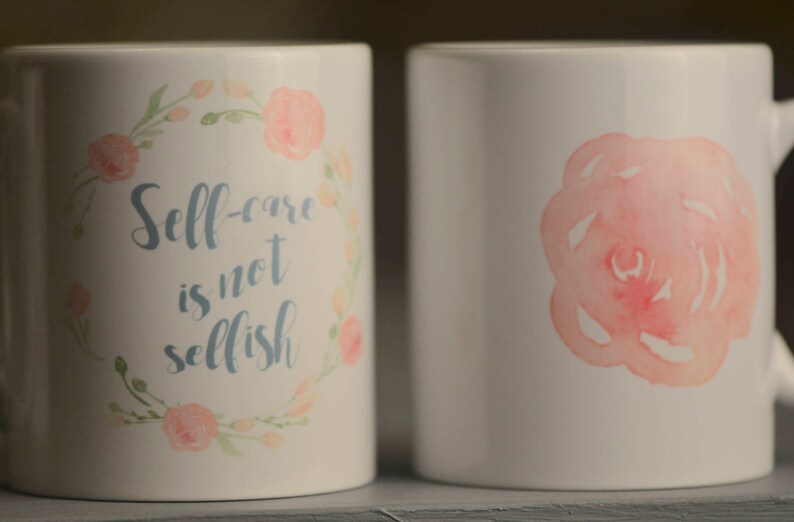May include: Two white ceramic mugs with floral designs. One mug has a pink watercolor rose on the front. The other mug has a floral wreath with the text "Self-care is not selfish".