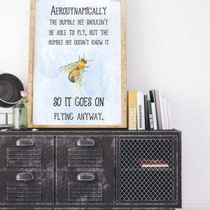 Op de afbeelding: Een motiverend citaat over een hommel, gedrukt op een lichtblauwe achtergrond met een aquareleffect. Het citaat luidt: "Aerodynamisch gezien zou de hommel niet kunnen vliegen, maar de hommel weet het niet, dus hij vliegt gewoon door."